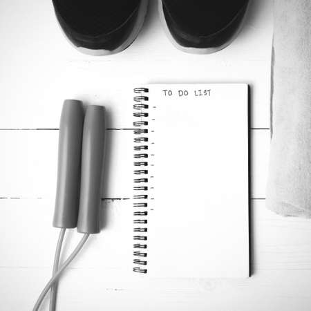 fitness equipment : running shoes,towel,jumping rope and notebook write to do list on white wood table black and white color tone styleの写真素材