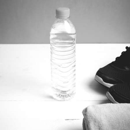 fitness equipment: towel,drinking water and running shoes on white wood table black and white color styleの写真素材