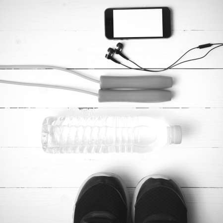 fitness equipment : running shoes,jumping rope,water bottle and phone on white wood table black and white color tone styleの写真素材