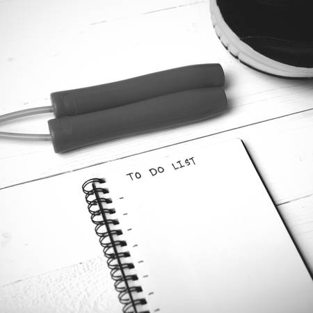 fitness equipment : running shoes,jumping rope and notebook write to do list on white wood table...