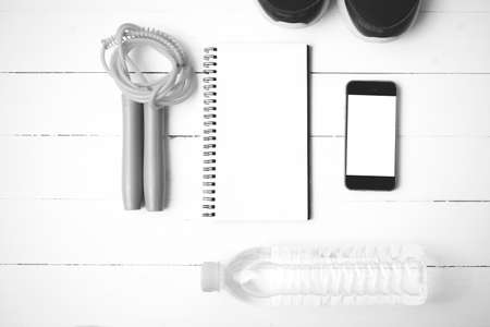 fitness equipment : running shoes,jumping rope,drinking water,notebook and phone on white wood table  black and white tone color styleの写真素材
