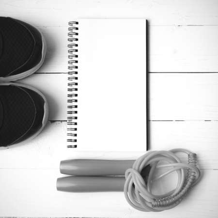 fitness equipment : running shoes,jumping rope and notepad on white wood table black and white color tone styleの写真素材