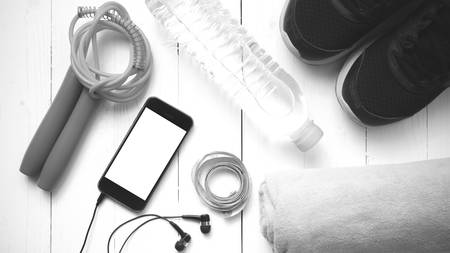 fitness equipment : running shoes,towel,jumping rope,water bottle,phone and measuring tape on white wood table black and white color tone styleの写真素材