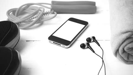 fitness equipment : running shoes,towel,jumping rope and phone on white wood table black and white...