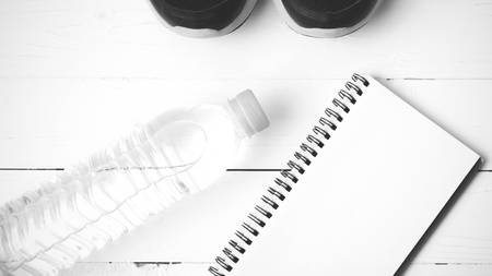fitness equipment : running shoes,drinking water and notebook on white wood table black and white...