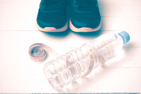 fitness equipment : running shoes,drinking water and measuring tape on white wood table vintage styleの写真素材