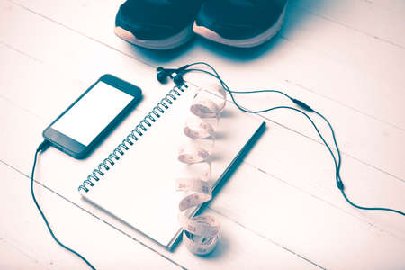running shoes,measuring tape,notebook and phone on white wood table vintage style