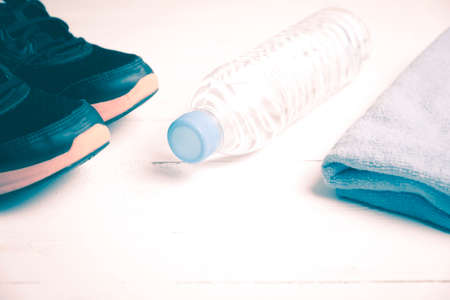 fitness equipment:blue towel,drinking water and running shoes on white wood table vintage style