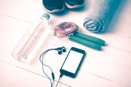 fitness equipment : running shoes,towel,jumping rope,water bottle and phone on white wood table...