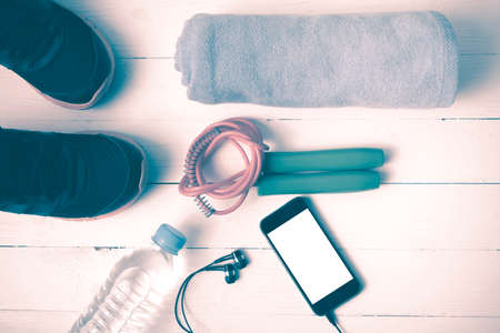 fitness equipment : running shoes,towel,jumping rope,water bottle and phone on white wood table...