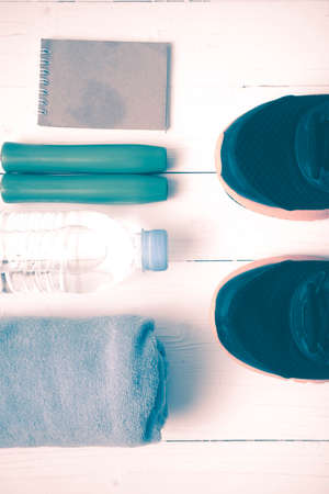 fitness equipment : running shoes,towel,jumping rope,water bottle and notepad on white wood table...