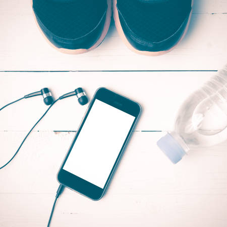 fitness equipment : running shoes,drinking water and phone on white wood table vintage styleの写真素材