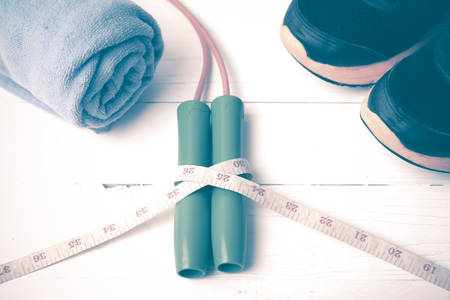 fitness equipment : running shoes,towel,jumping rope and measuring tape on white wood table vintage...