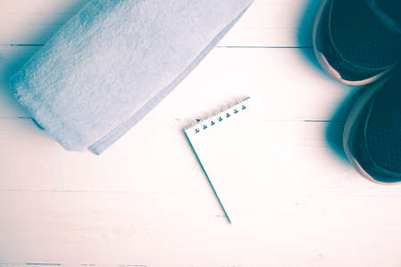 fitness equipment : running shoes,blue towel and notepad on white wood table vintage style
