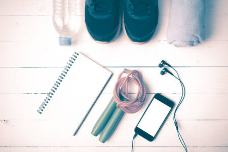 fitness equipment : running shoes,towel,jumping rope,water bottle,phone and notepad on white wood...