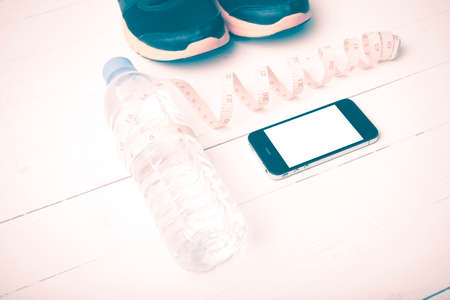 fitness equipment : running shoes,drinking water,measuring tape and phone on white wood table...