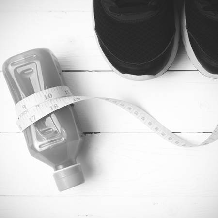 running shoes,orange juice and measuring tape on white wood background black and white tone color...