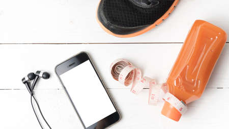 running shoes,orange juice,measuring tape and phone on white wood background