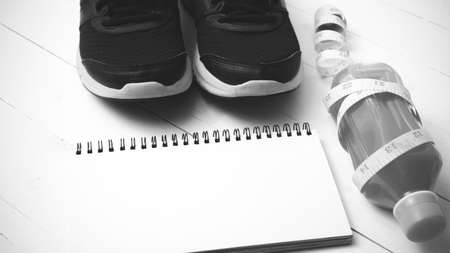 running shoes,orange juice,measuring tape and notepad on white wood background black and white tone...