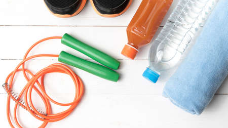 fitness equipment : running shoes,towel,jumping rope,drinking water and orange juice on white wood backgroundの写真素材