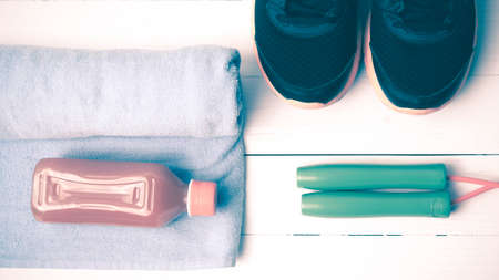 fitness equipment : running shoes,towel,jumping rope and orange juice on white wood background vintage tone styleの写真素材