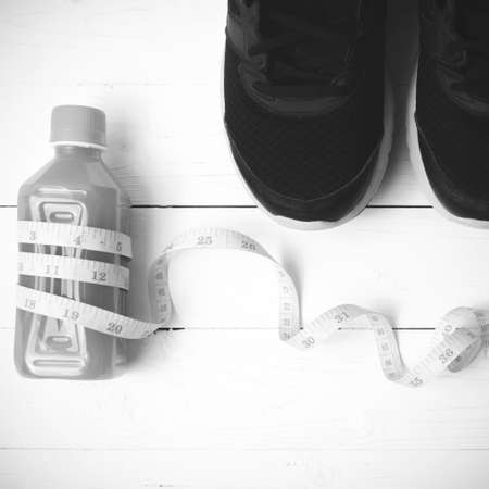 running shoes,orange juice and measuring tape on white wood background black and white tone color...