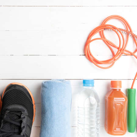 fitness equipment : running shoes,towel,jumping rope,drinking water and orange juice on white wood backgroundの写真素材