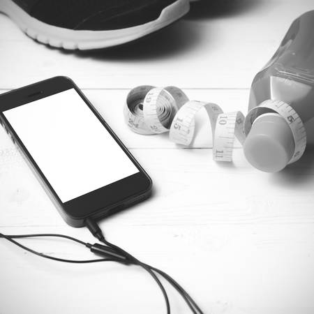running shoes,orange juice,measuring tape and phone on white wood background black and white tone color styleの写真素材