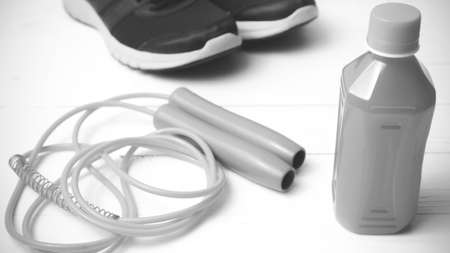 fitness equipment : running shoes,jumping rope and orange juice on white wood background black and...