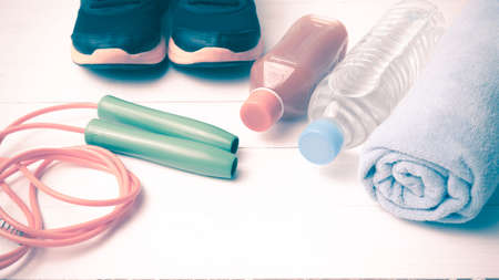 fitness equipment : running shoes,towel,jumping rope,drinking water and orange juice on white wood background vintage tone styleの写真素材