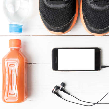 running shoes,orange juice,drinking water and phone on white wood background