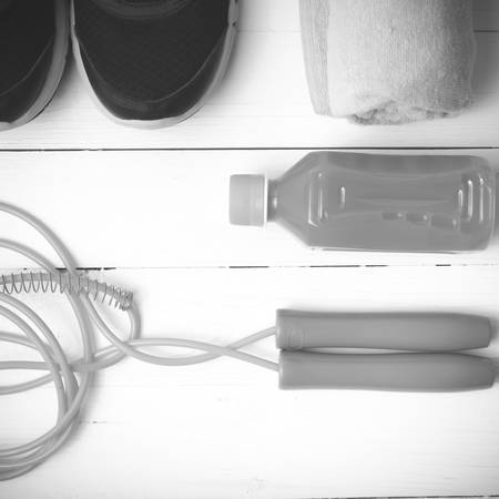 fitness equipment : running shoes,towel,jumping rope and orange juice on white wood background black and white tone color styleの写真素材