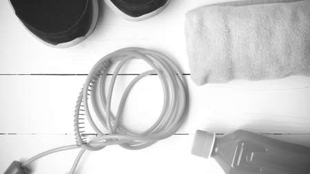 fitness equipment : running shoes,towel,jumping rope and orange juice on white wood background black and white tone color styleの写真素材
