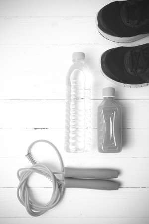 fitness equipment : running shoes,jumping rope,drinking water and orange juice on white wood background black and white tone color styleの写真素材