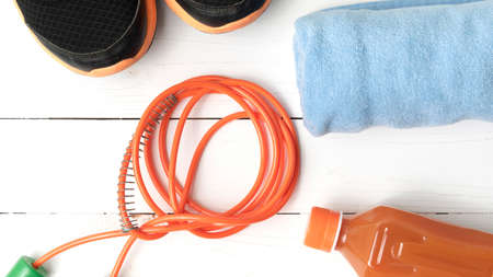 fitness equipment : running shoes,towel,jumping rope and orange juice on white wood backgroundの写真素材