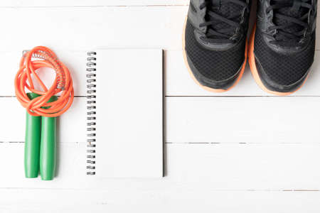 fitness equipment : running shoes,jumping rope and notepad on white wood table