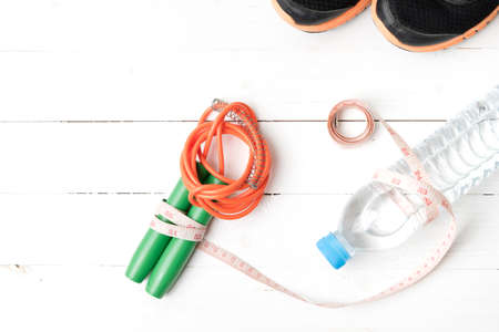 fitness equipment : running shoes,jumping rope,measuring tape and water bottle on white wood tableの写真素材