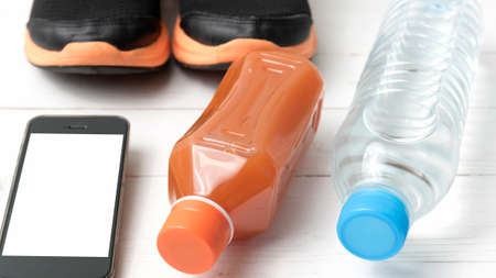 running shoes,orange juice,drinking water and phone on white wood background
