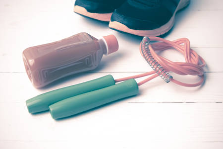 fitness equipment : running shoes,jumping rope and orange juice on white wood background vintage...