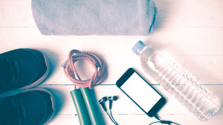 fitness equipment : running shoes,towel,jumping rope,water bottle and phone on white wood table vintage styleの写真素材