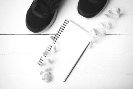 running shoes with notebook and measuring tape on white wood table black and white tone color styleの写真素材