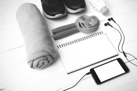 fitness equipment : running shoes,towel,jumping rope,water bottle,phone and notepad on white wood...