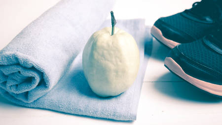 fitness equipment : running shoes,blue towel and guava fruit on white wood table vintage styleの写真素材