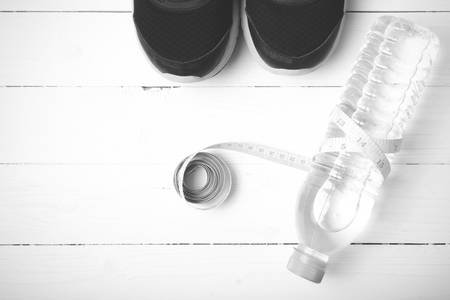 fitness equipment : running shoes,drinking water and measuring tape on white wood table black and white tone color styleの写真素材