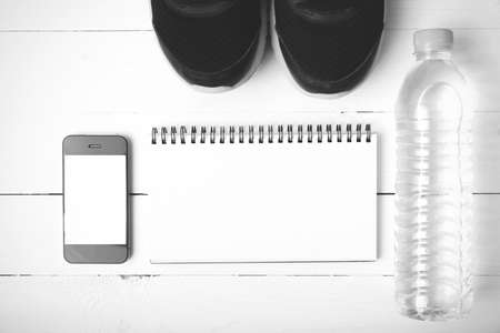 fitness equipment : running shoes,drinking water,notebook and phone on white wood table black and white tone color styleの写真素材