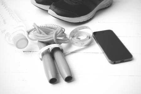 fitness equipment : running shoes,jumping rope,drinking water,measuring tape and phone on white wood table black and white tone color styleの写真素材