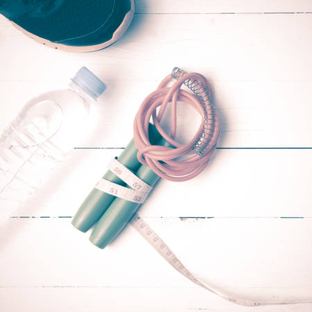 fitness equipment : running shoes,jumping rope,measuring tape and water bottle on white wood table...