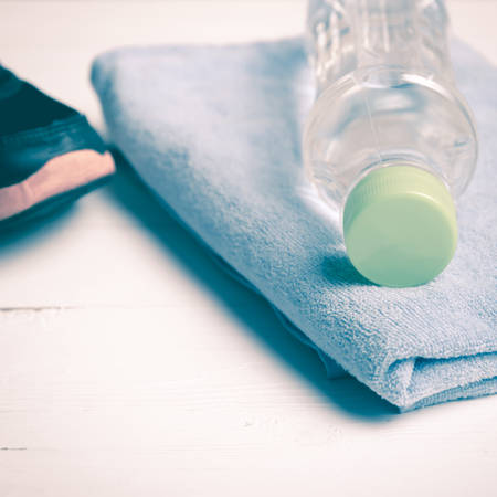 fitness equipment:blue towel,drinking water and running shoes on white wood table vintage styleの写真素材