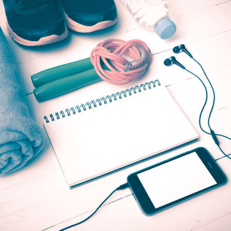 fitness equipment : running shoes,towel,jumping rope,water bottle,phone and notepad on white wood table vintage styleの写真素材