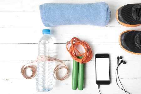 fitness equipment : running shoes,towel,jumping rope,water bottle,phone and measuring tape on white wood tableの写真素材